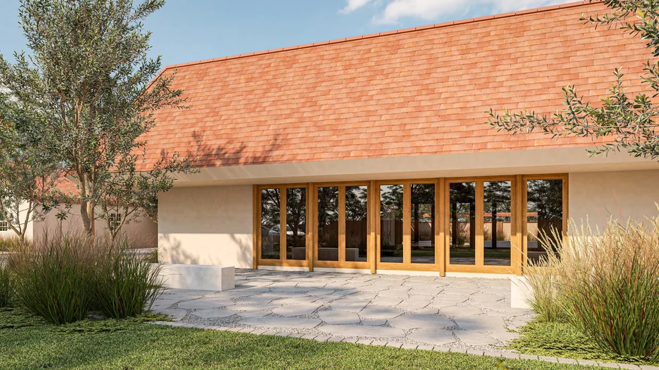 Rendering of a red tile roof building with a wall of wood-framed glass doors opening onto a flagstone patio, bordered by tall ornamental grasses and lawn.