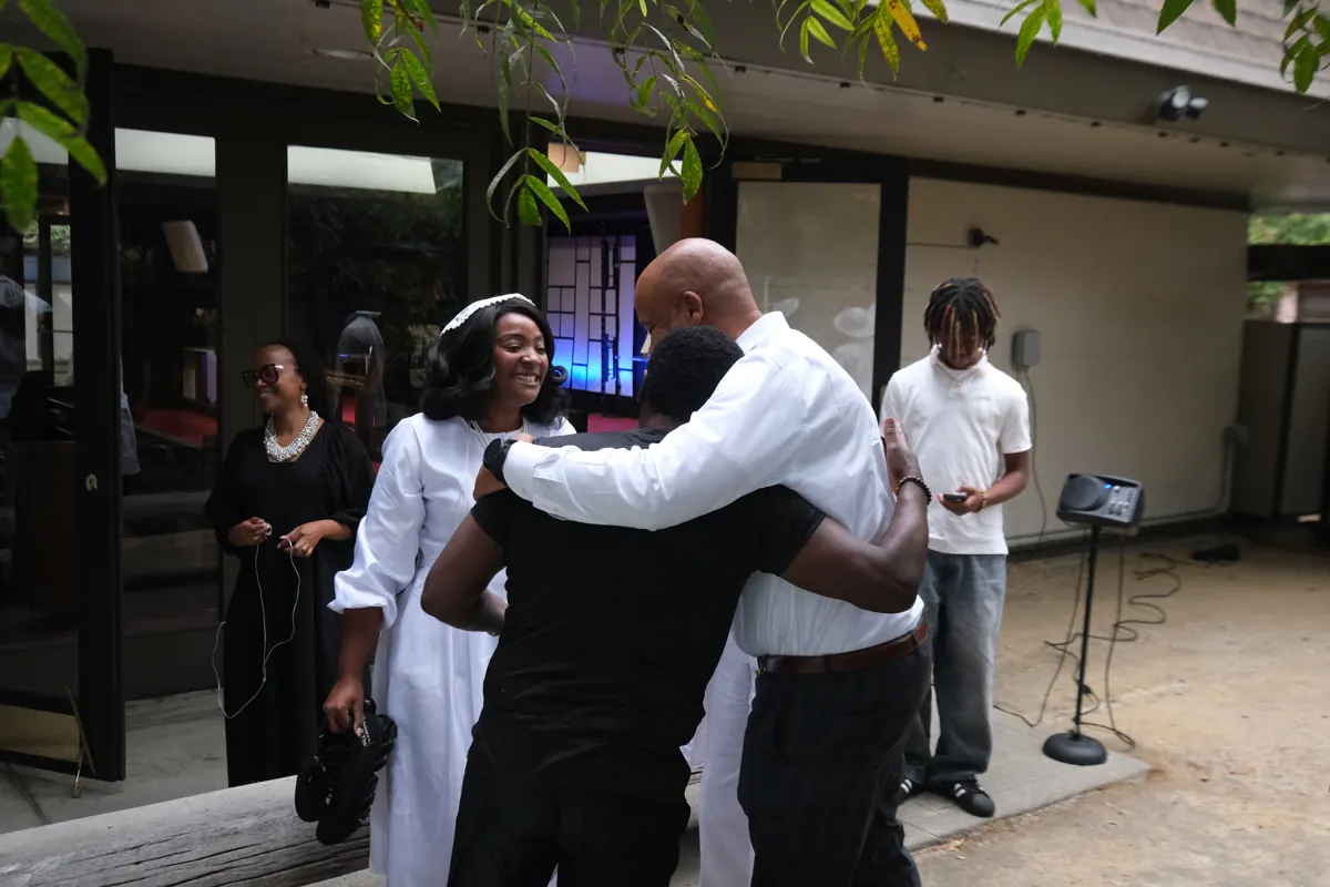 Two people embrace outside the church with other guests nearby.