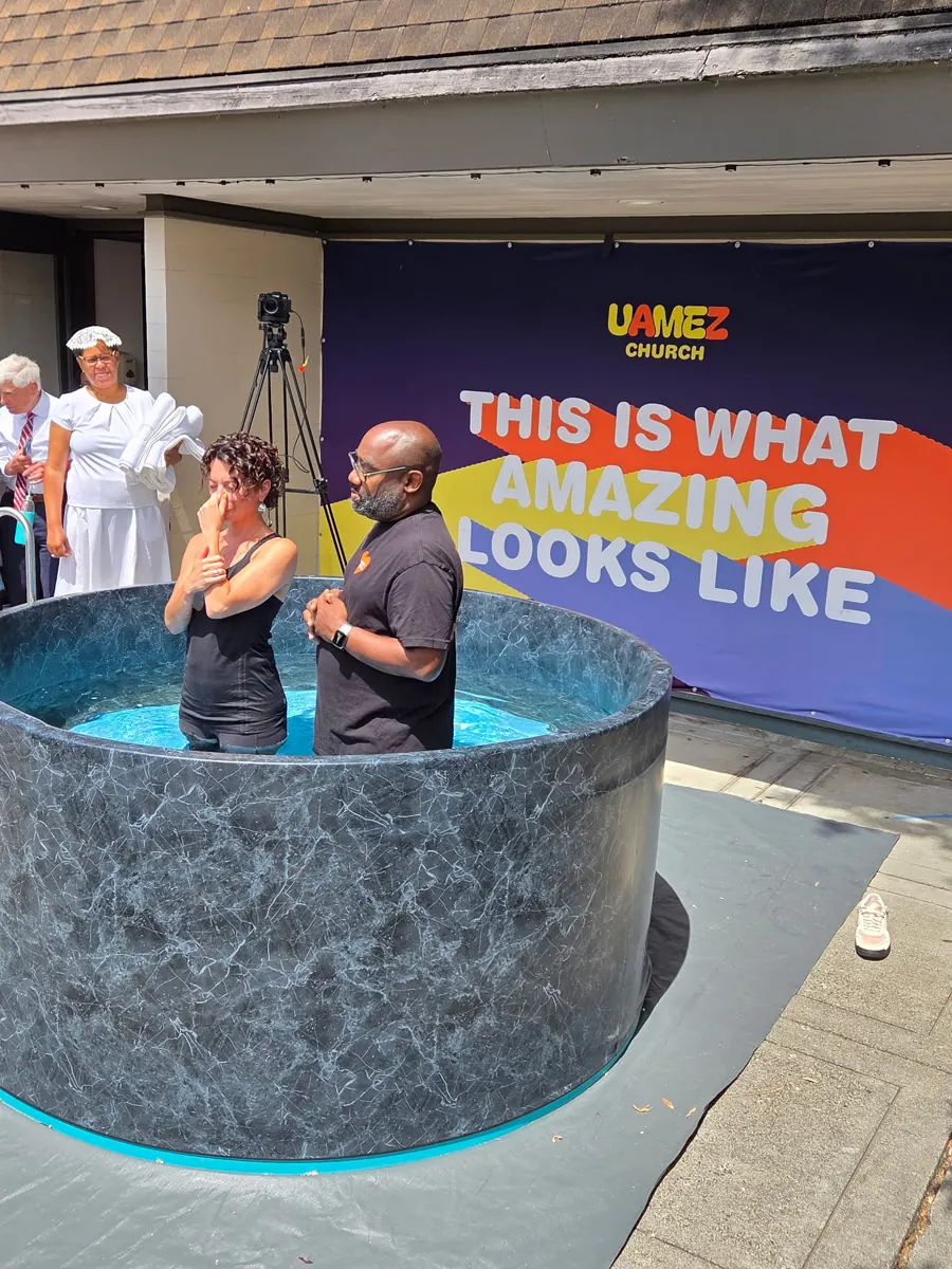People stand beside a baptism pool inside the sanctuary, with a church banner behind them.