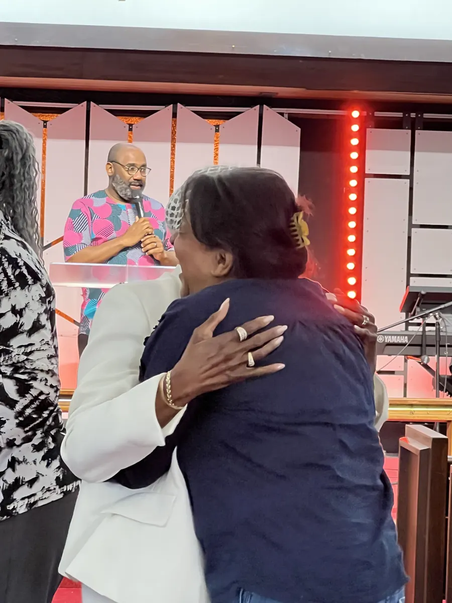 Two people embrace warmly near the front of the sanctuary.