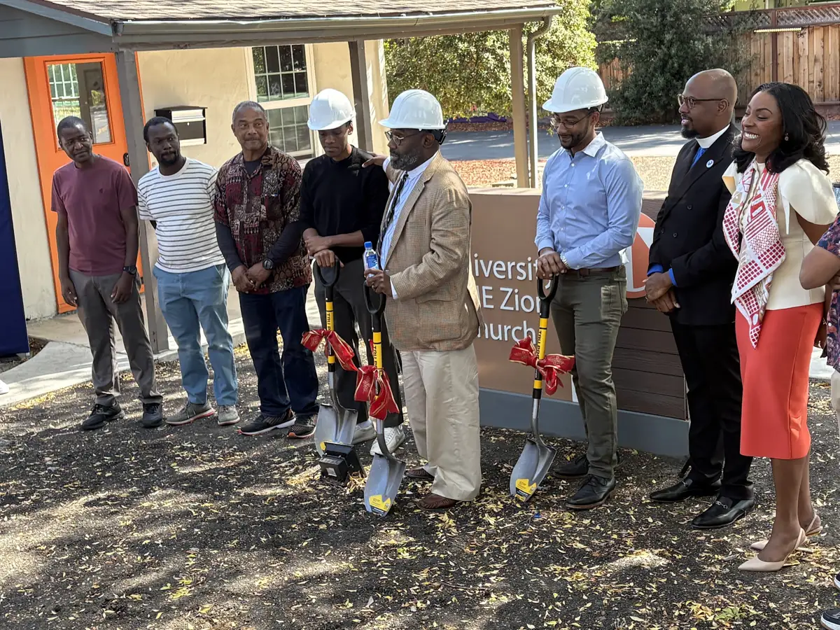 People gather beside the church sign, with three wearing white hard hats and holding ceremonial shovels.