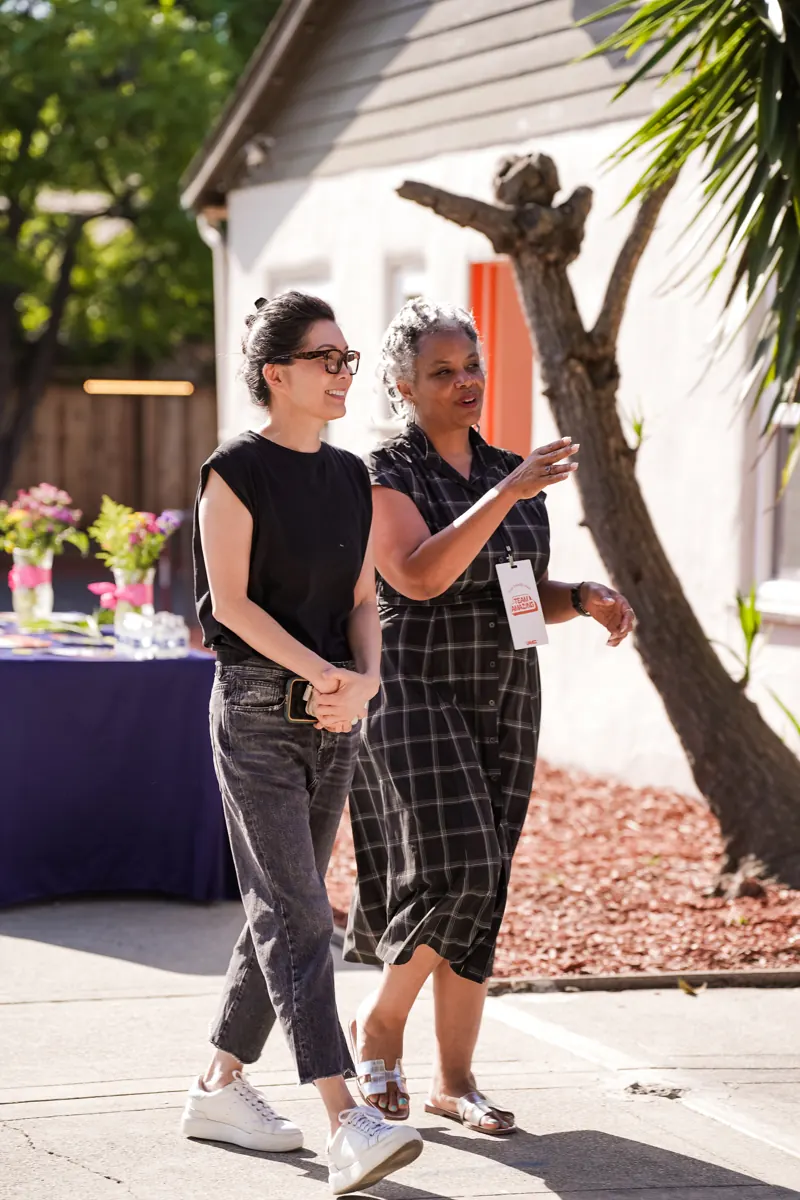 Two people walk and talk together in the sunny church courtyard.