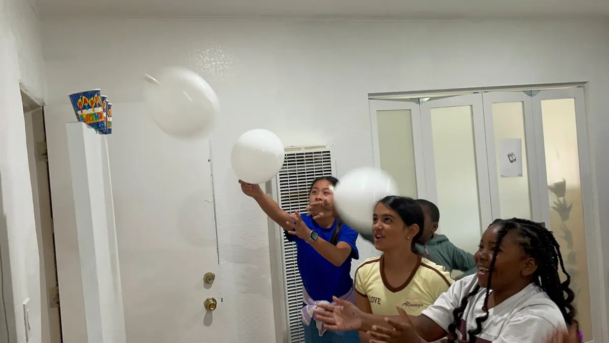 Children and an adult play with white balloons together in a classroom.