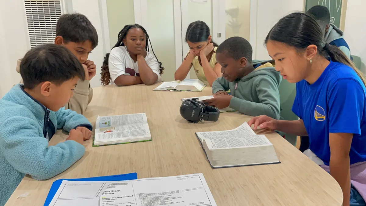 Children read open books together around a classroom table.