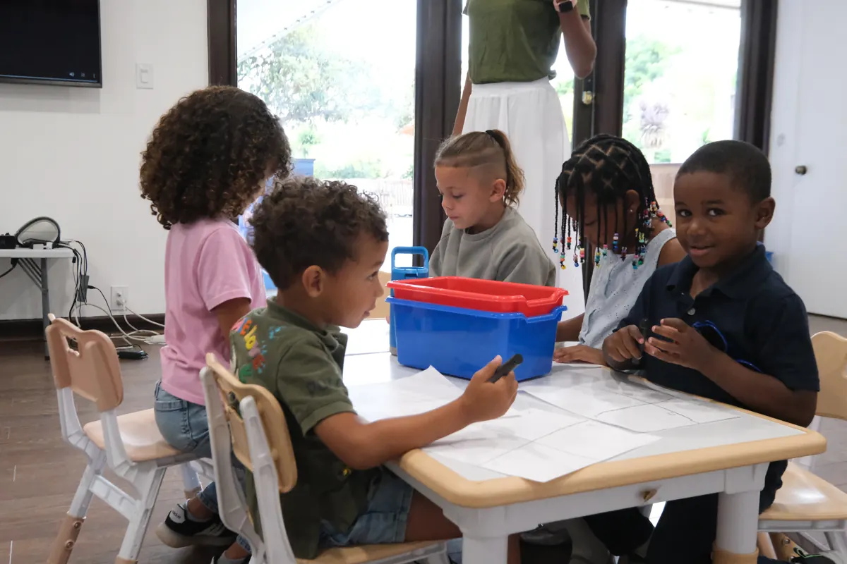 Children work together on a paper activity at a classroom table.