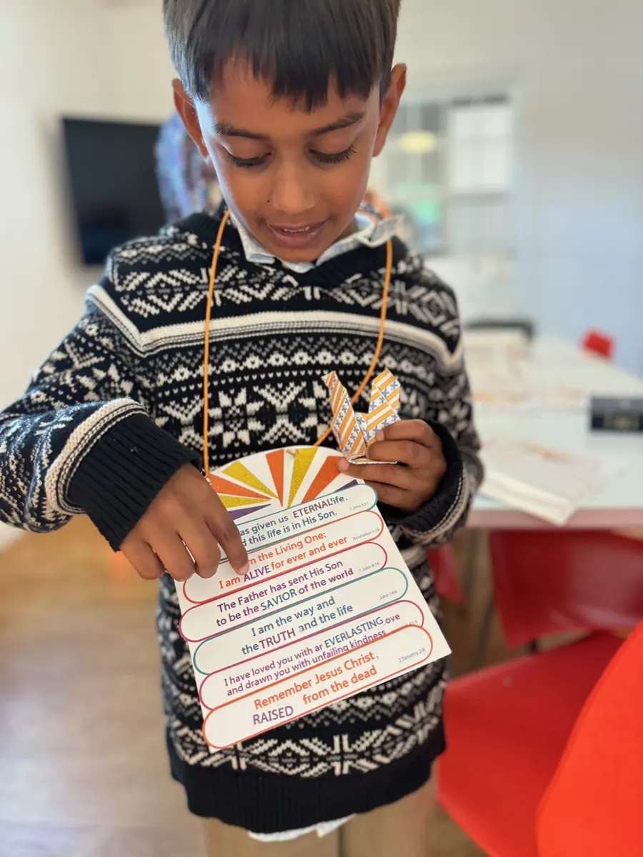 A child holds up a colorful paper craft made during an Amazing Kids activity.