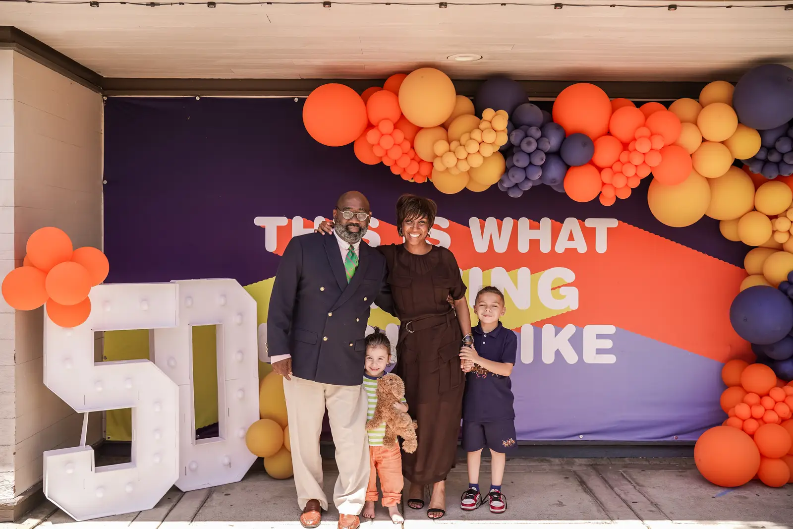 Pastor Kaloma Smith and his family stand together in front of a colorful balloon display.