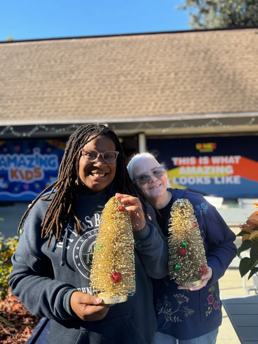 Two people smile while holding decorative greenery outside the church.