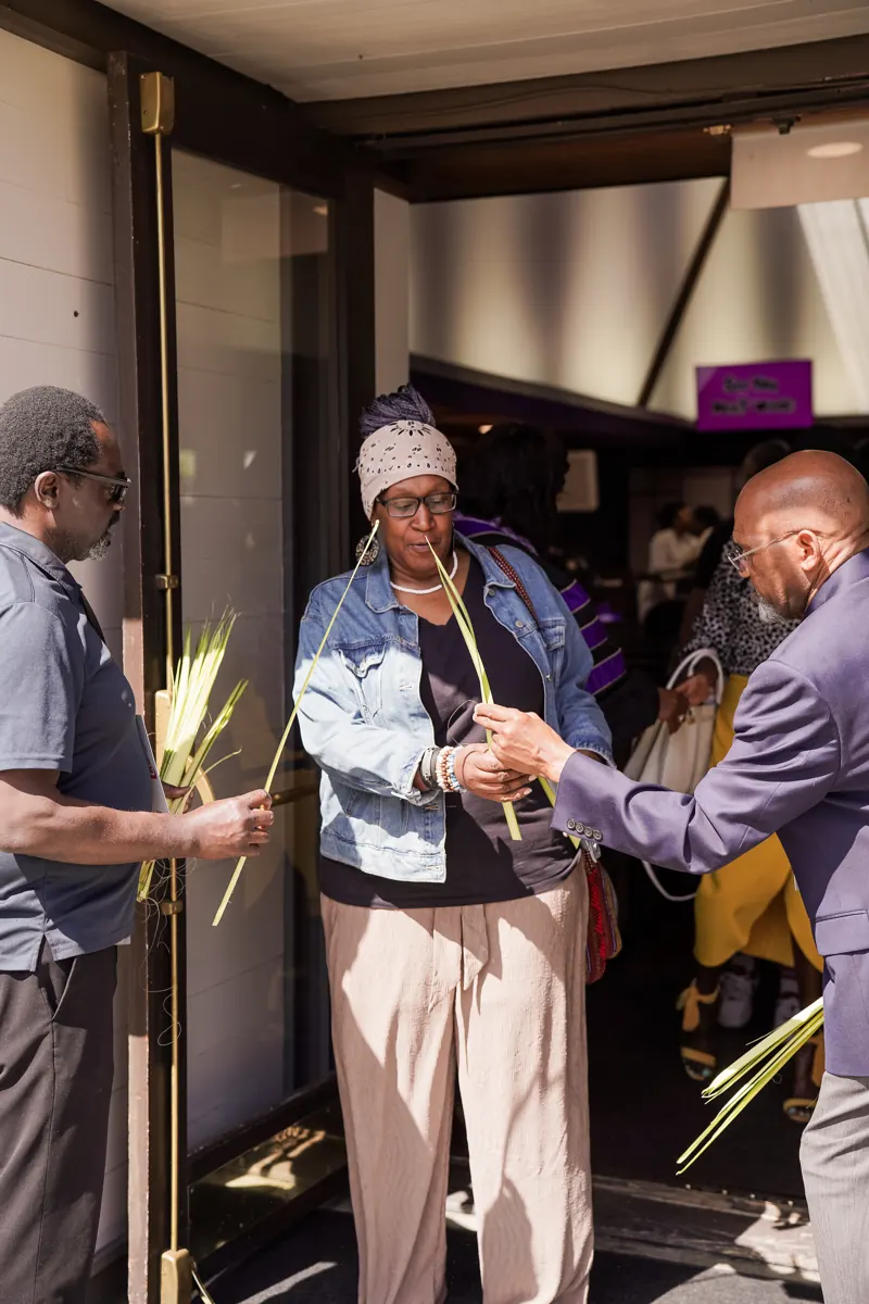 People hand palm branches to guests at the sanctuary doorway.