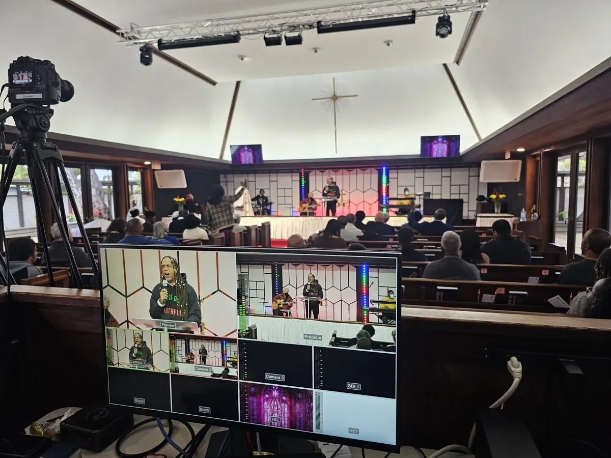 A camera and video switching screens stand at the back of the sanctuary during a service.