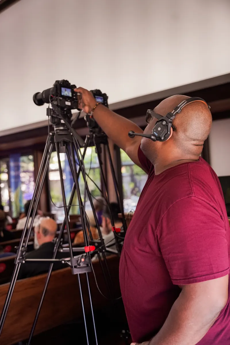 A person wearing headphones operates a tripod-mounted camera during a service.