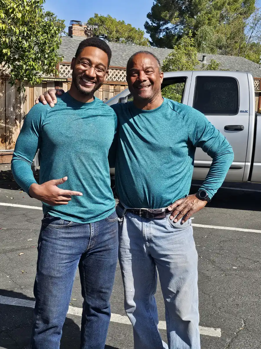 Two smiling volunteers in teal shirts stand together outside beside a parked truck.