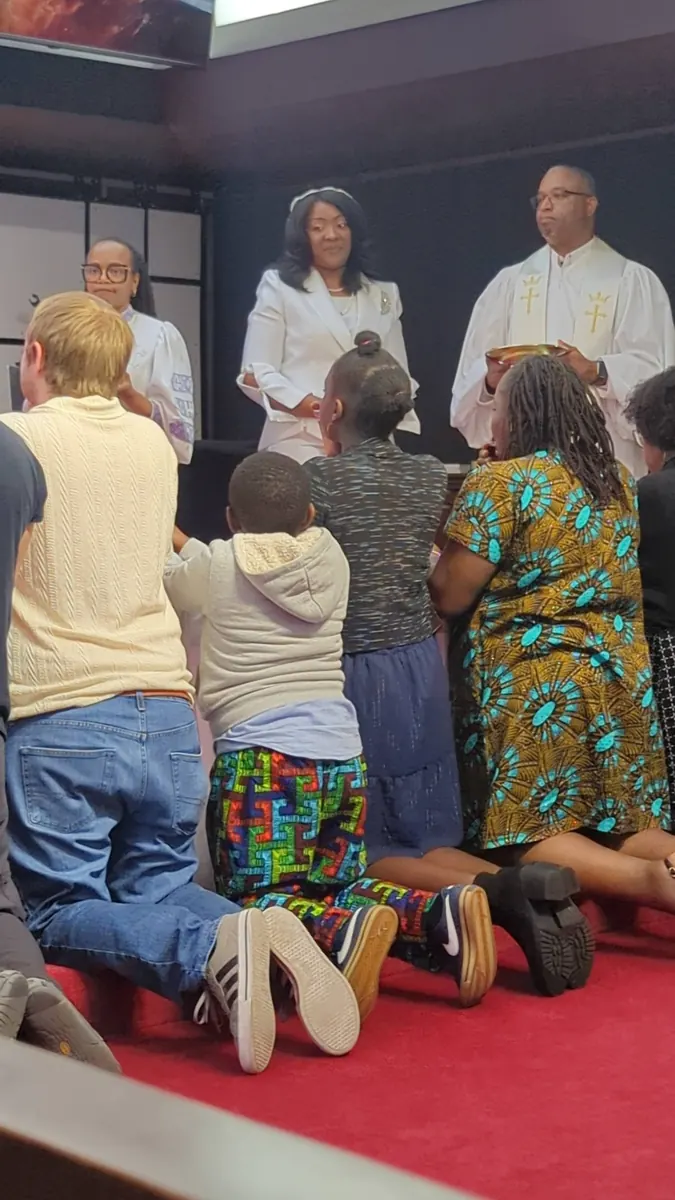 People kneel at the altar rail as others stand with them near the front of the sanctuary.
