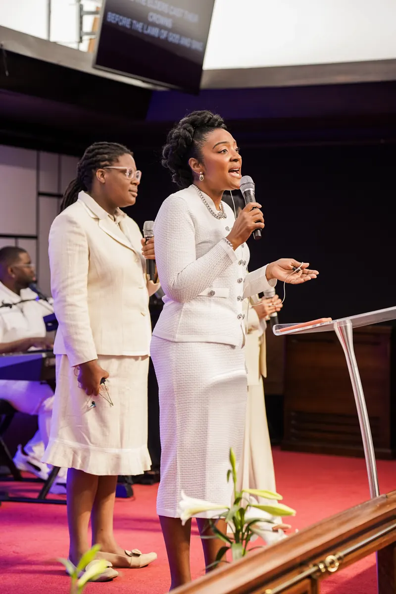 Two women in white sing into microphones at the front of the sanctuary.