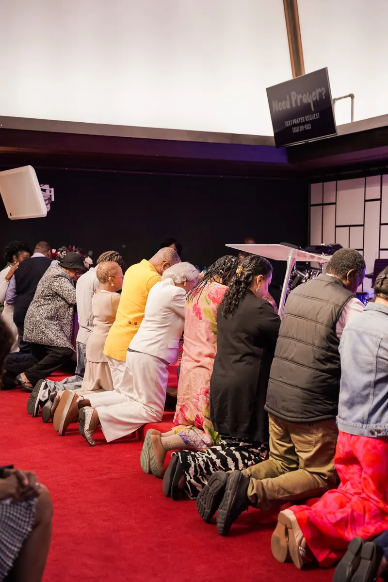 People kneel together at the altar rail while others stand nearby in the sanctuary.