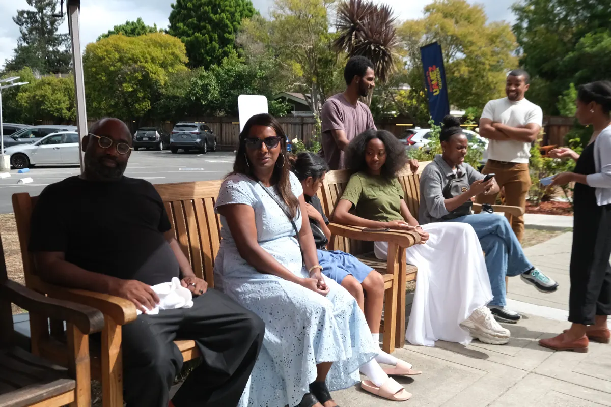 People sit and talk together on wooden benches in the church courtyard.