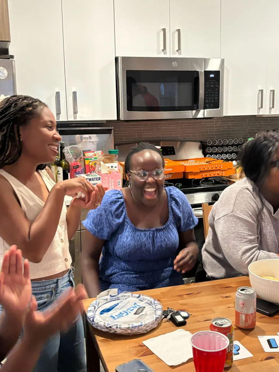 Friends laugh together over food at a kitchen table.